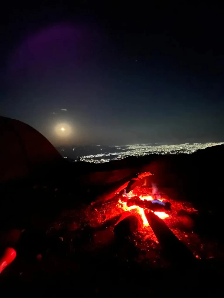 Bonfire embers with city lights and moon